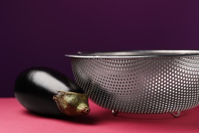 Photo of Colander with fresh eggplant on color background, closeup