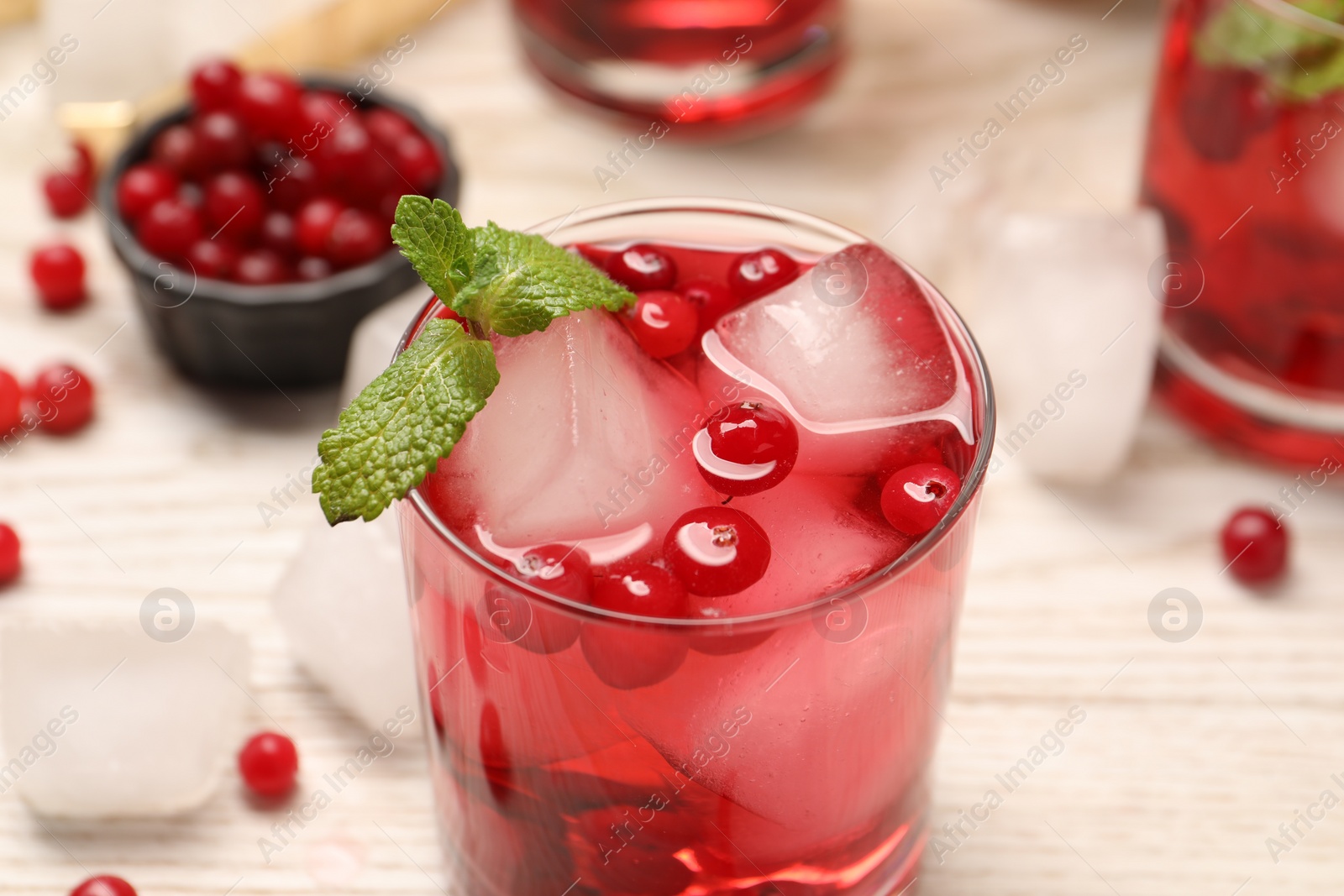 Photo of Tasty cranberry cocktail with ice cubes and mint in glass on light table, closeup