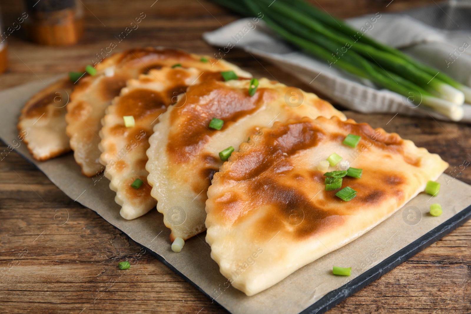 Photo of Board with delicious fried chebureki on wooden table, closeup