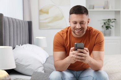 Handsome man sending message via smartphone on bed at home. Space for text