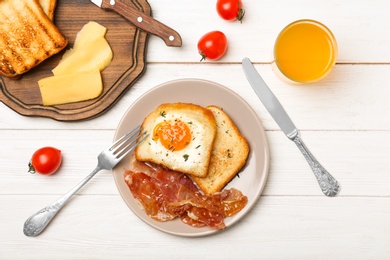 Photo of Plate with fried egg, bacon and toasts on white wooden background