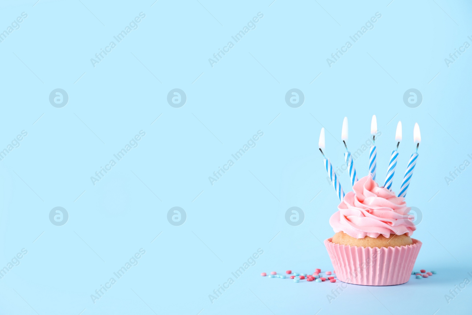 Photo of Delicious birthday cupcake with burning candles and sprinkles on light blue background, space for text