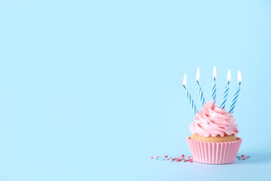 Delicious birthday cupcake with burning candles and sprinkles on light blue background, space for text