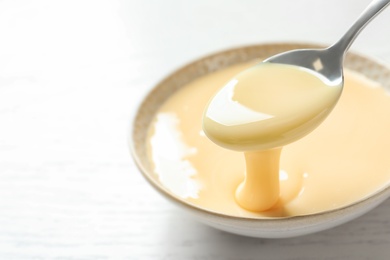 Spoon of pouring condensed milk over bowl on table, closeup with space for text. Dairy products