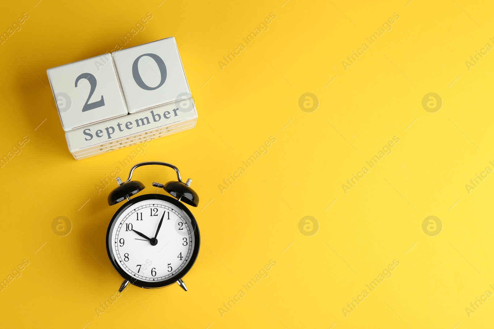 Photo of Wooden block calendar and alarm clock on yellow background, flat lay. Space for text