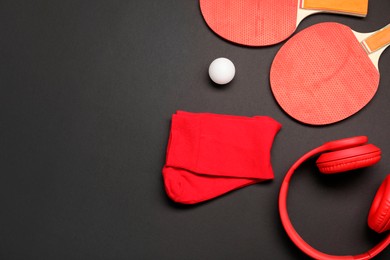 Sports equipment. Ping pong rackets, ball, headphones and socks on black background, flat lay. Space for text