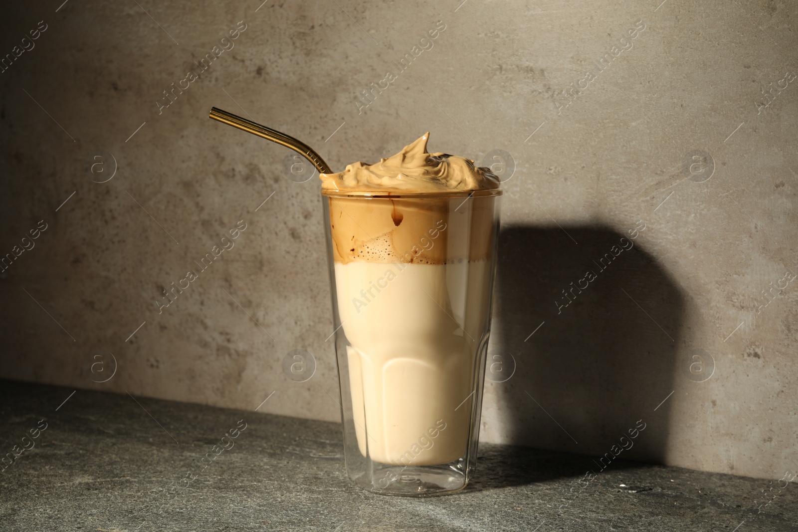 Photo of Glass of delicious dalgona coffee on grey textured table