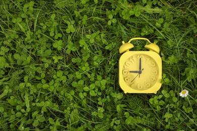 Yellow alarm clock on green grass outdoors, top view. Space for text