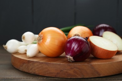 Photo of Board with different kinds of onions on wooden table, closeup