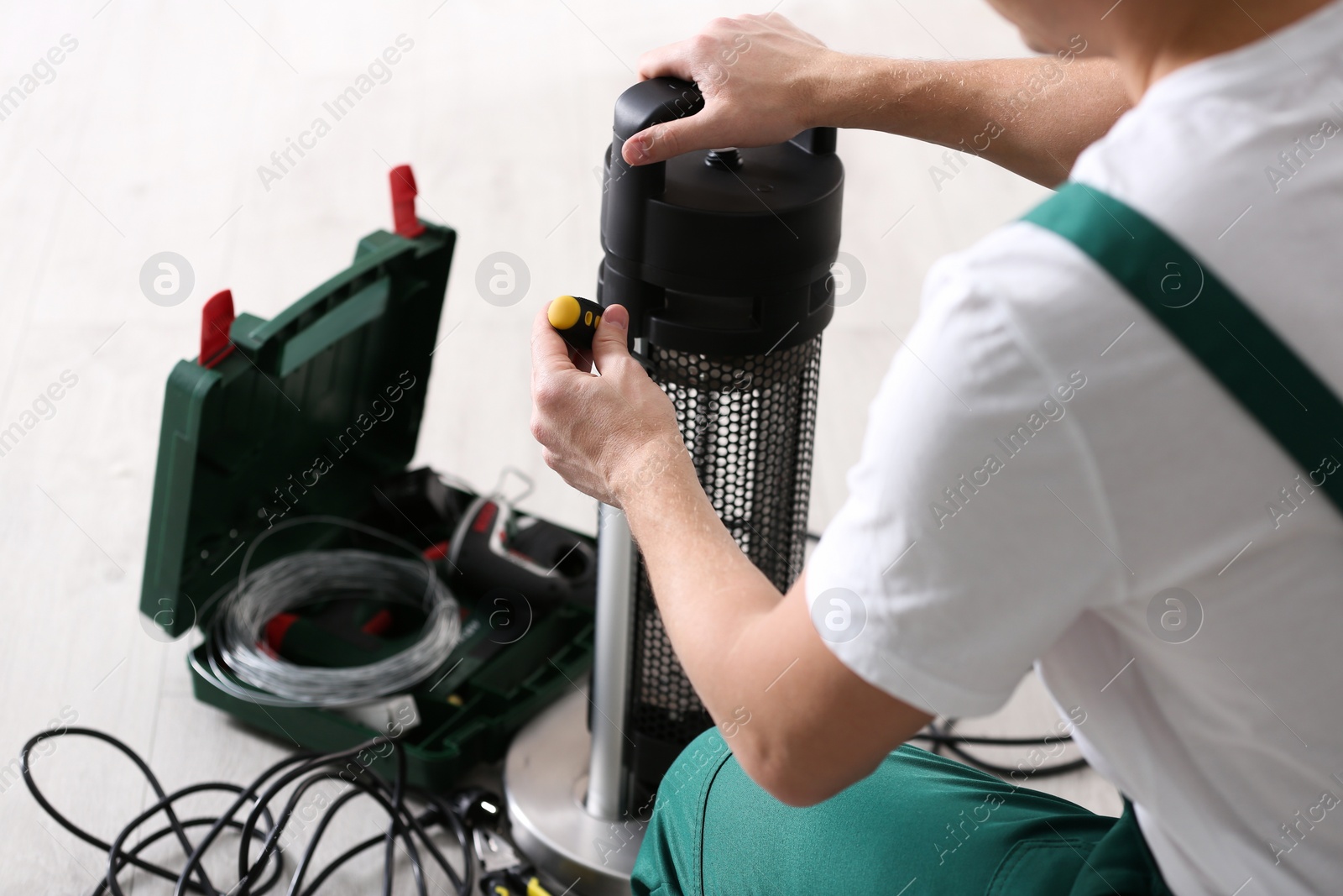 Photo of Professional technician repairing electric patio heater with screwdriver indoors, closeup