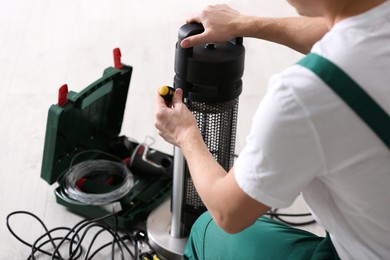 Photo of Professional technician repairing electric patio heater with screwdriver indoors, closeup