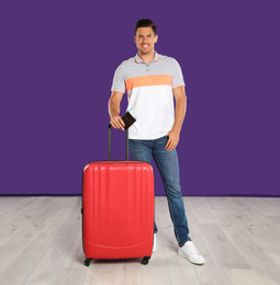 Handsome man with suitcase and ticket in passport for summer trip near purple wall. Vacation travel