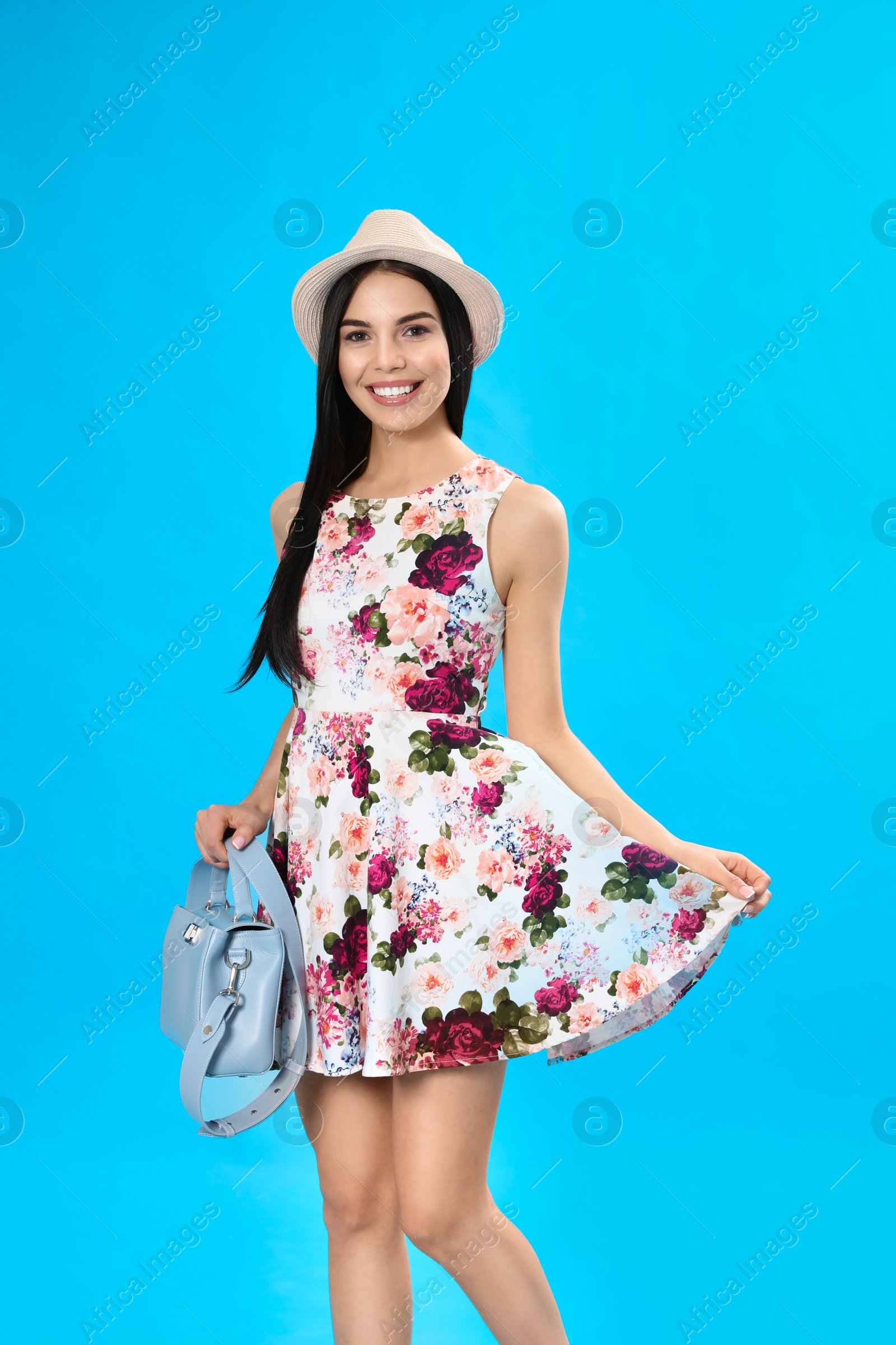 Photo of Young woman wearing floral print dress with stylish handbag on light blue background