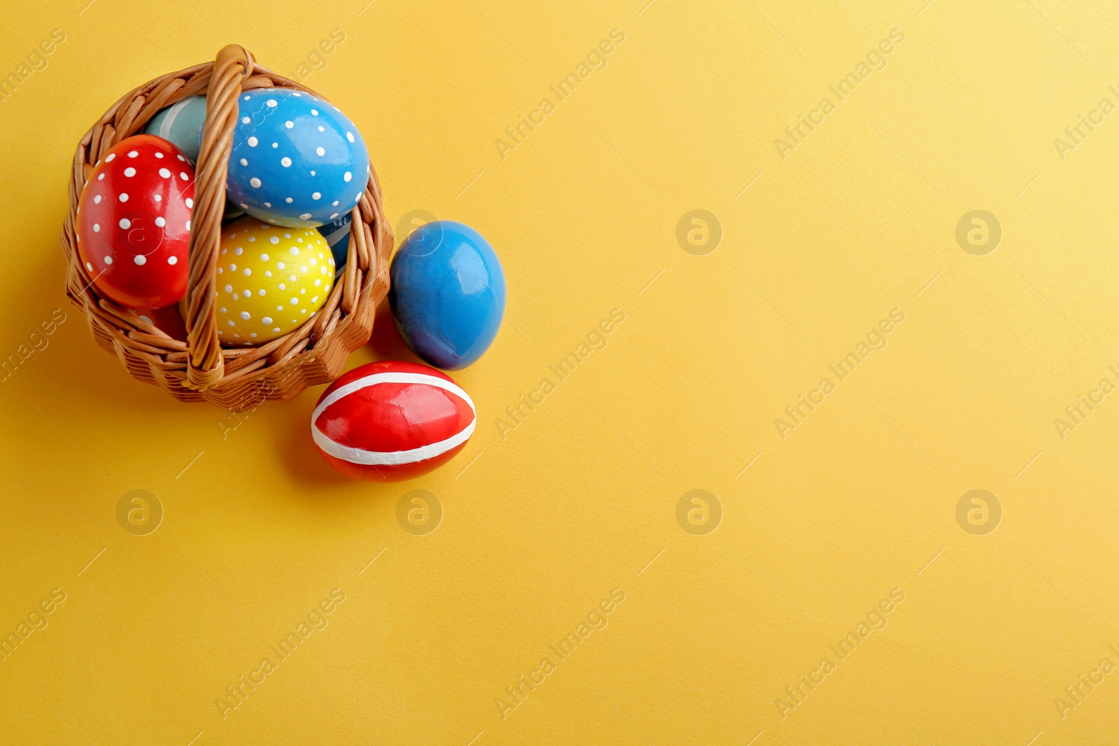 Photo of Wicker basket with painted Easter eggs on color background, top view. Space for text