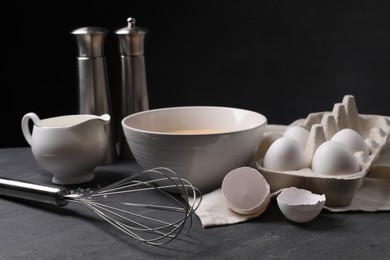 Photo of Metal whisk and dough ingredients on dark grey table