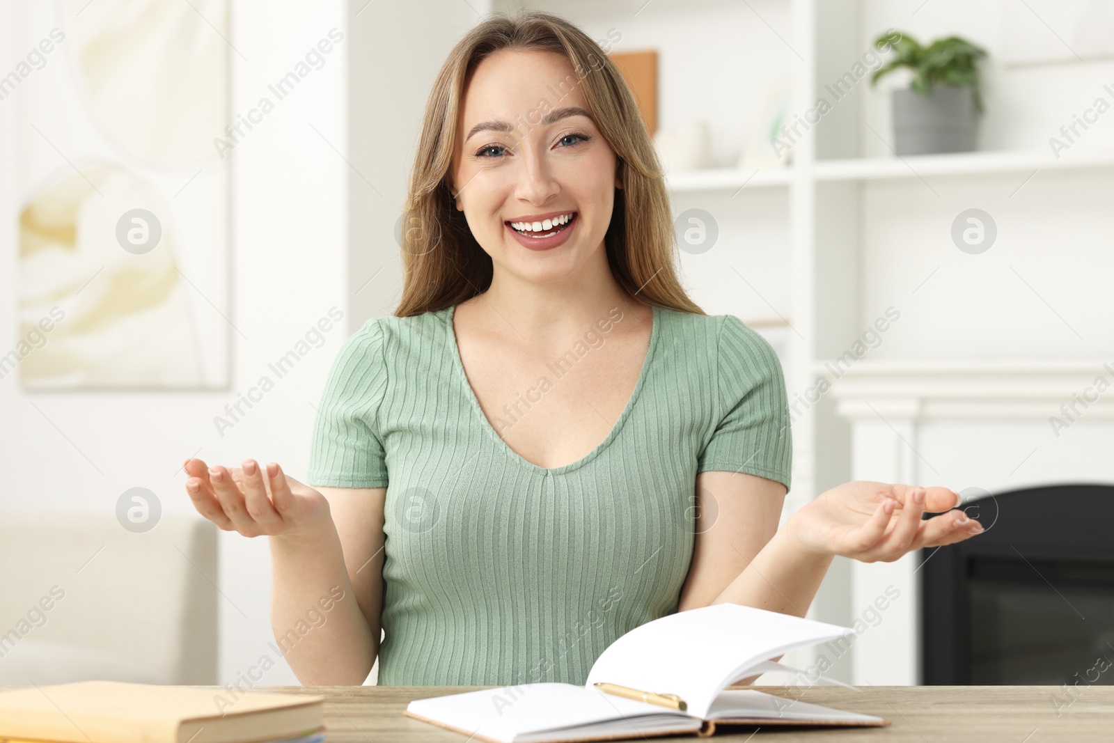 Photo of Young woman waving hello during video chat at wooden table indoors, view from webcam