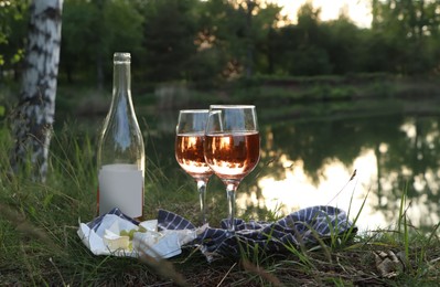 Delicious rose wine, cheese and grapes on picnic blanket near lake