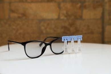 Single dose eye drops and glasses on white table