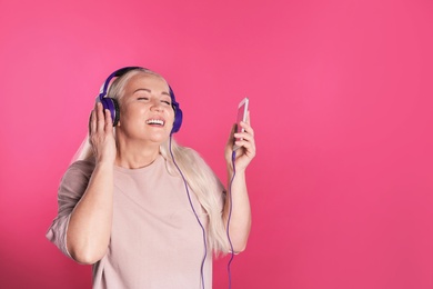 Mature woman in headphones with mobile device on color background. Space for text