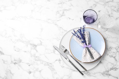 Cutlery, napkin, plates, glasses and preserved lavender flowers on white marble table, flat lay. Space for text