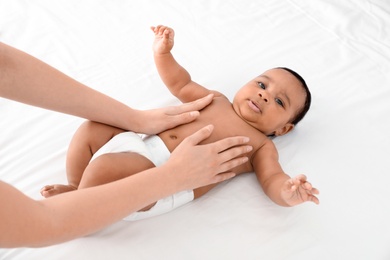 Photo of Mother and her cute child on white bed, above view. Baby massage and exercises