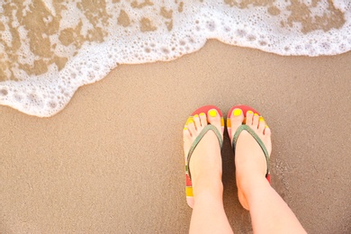 Photo of Top view of woman with stylish flip flops on sand near sea, space for text. Beach accessories