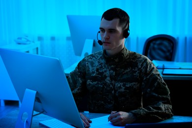 Image of Military service. Soldier in headphones working at table in office at night