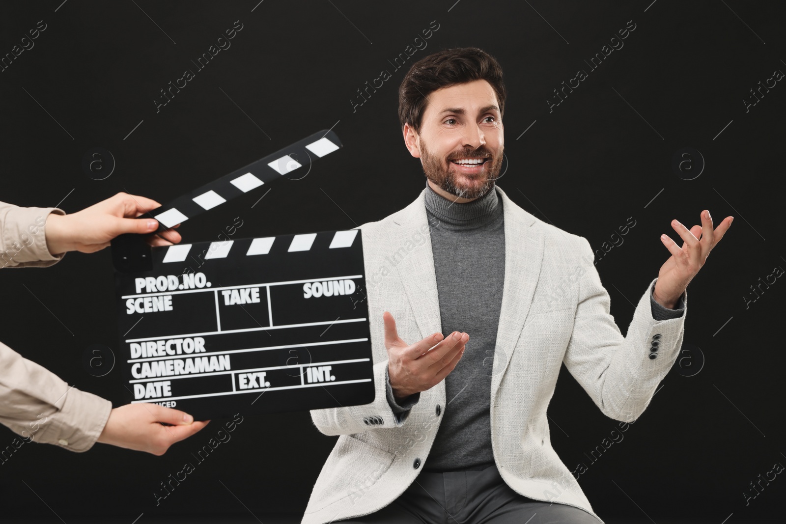 Photo of Actor performing while second assistant camera holding clapperboard on black background