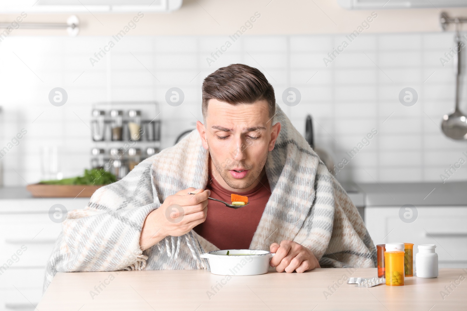 Photo of Sick young man eating broth to cure cold at table in kitchen