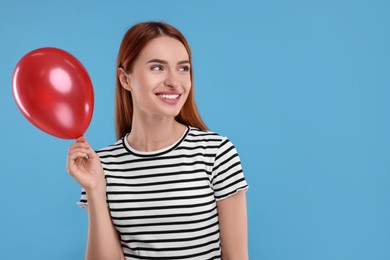 Photo of Happy woman with red balloon on light blue background, space for text