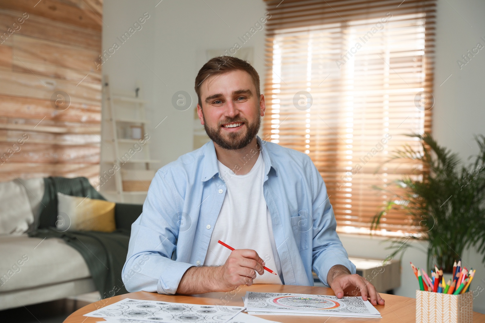 Photo of Young man coloring antistress picture at table indoors