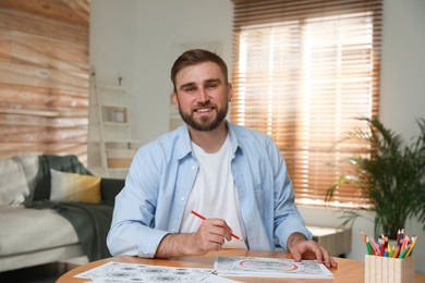 Photo of Young man coloring antistress picture at table indoors