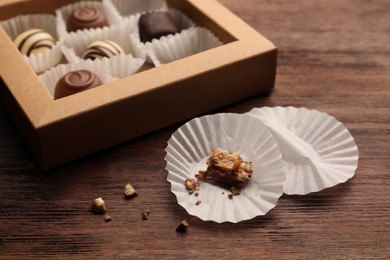 Candy paper cups near partially empty box of chocolate sweets on wooden table, closeup