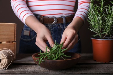 Photo of Woman with green rosemary sprigs at wooden table, closeup