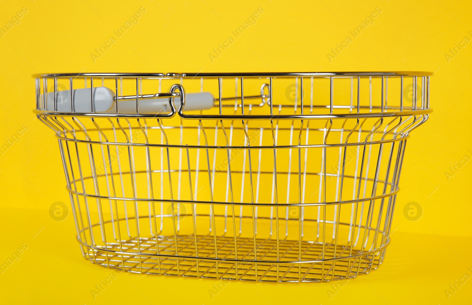 Photo of Empty metal shopping basket on yellow background