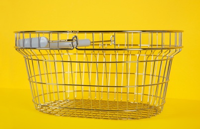 Photo of Empty metal shopping basket on yellow background