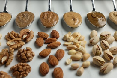 Photo of Tasty nut butters in spoons and raw nuts on white table, closeup