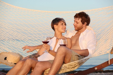 Photo of Young couple resting with glasses of wine in hammock on beach