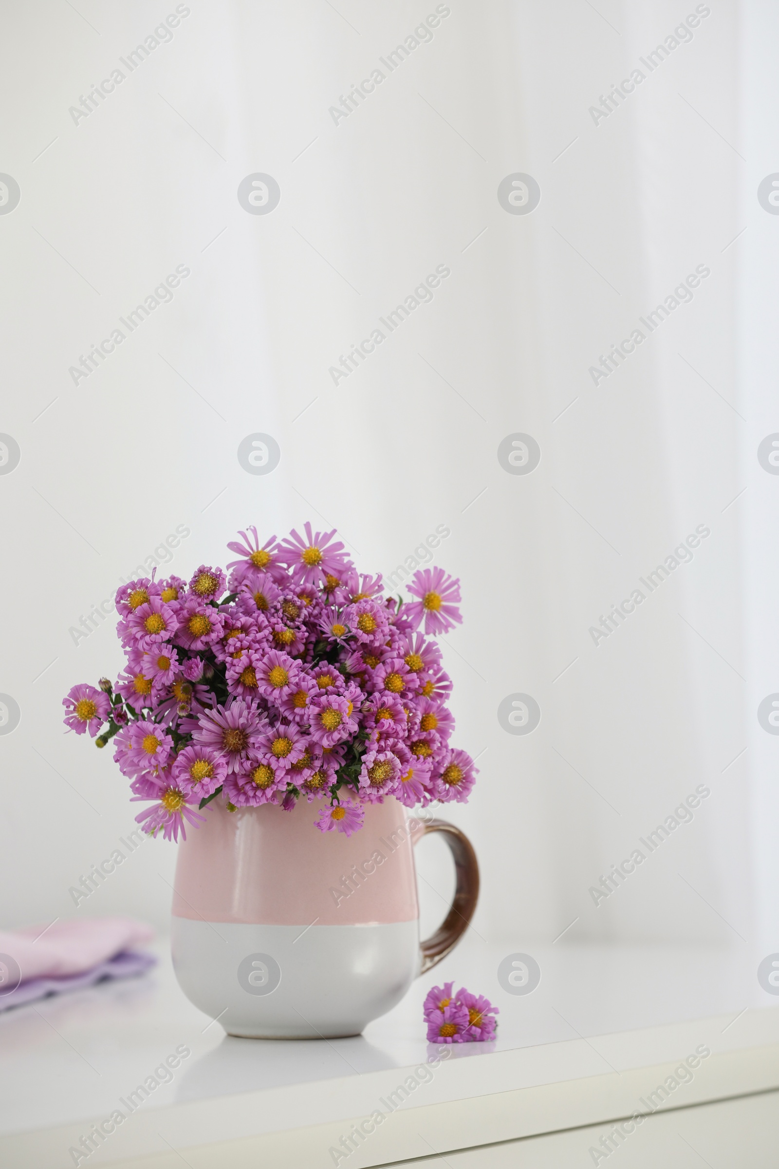 Photo of Cup with beautiful flowers on white table in light room