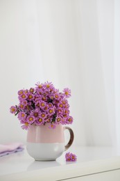 Photo of Cup with beautiful flowers on white table in light room