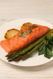 Photo of Tasty grilled salmon with asparagus and lemon on white wooden table, closeup