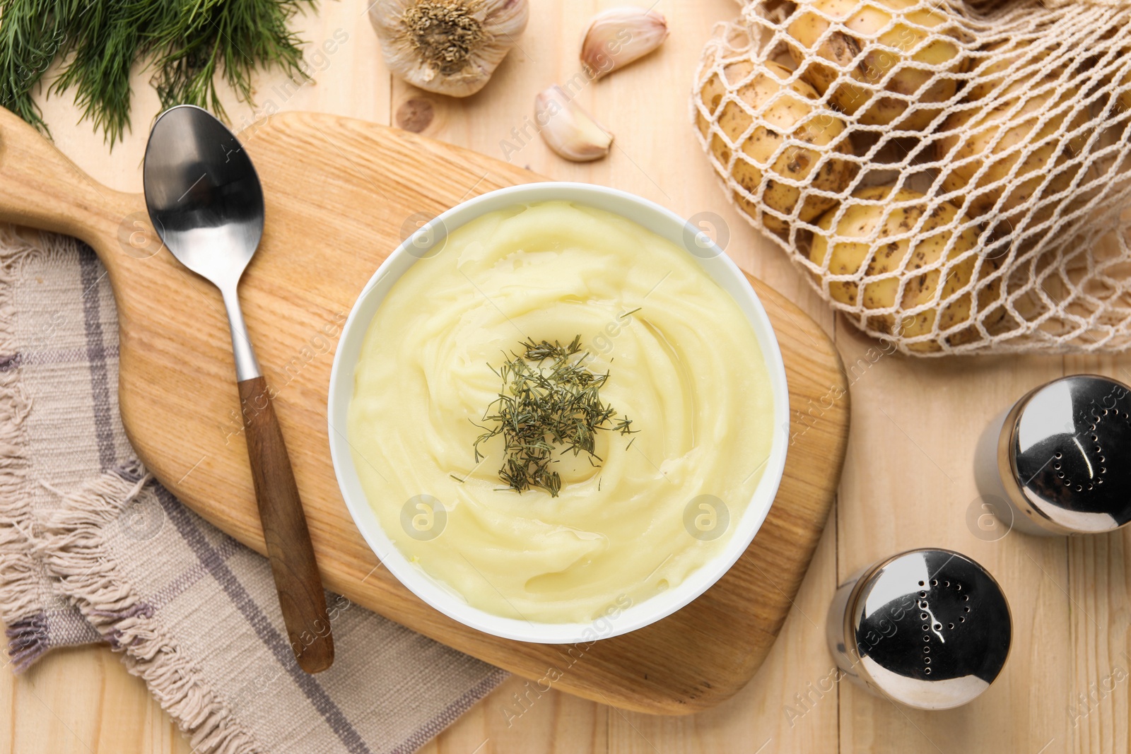 Photo of Bowl of tasty cream soup with dill, spoon and garlic on wooden table, flat lay