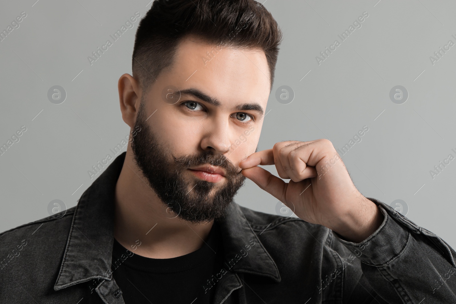 Photo of Young man touching mustache on grey background