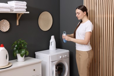 Photo of Woman pouring detergent into cap in laundry room