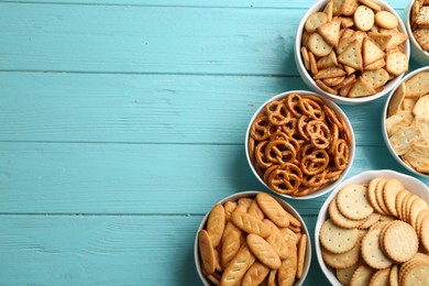 Different delicious crackers in bowls on turquoise wooden table, flat lay. Space for text