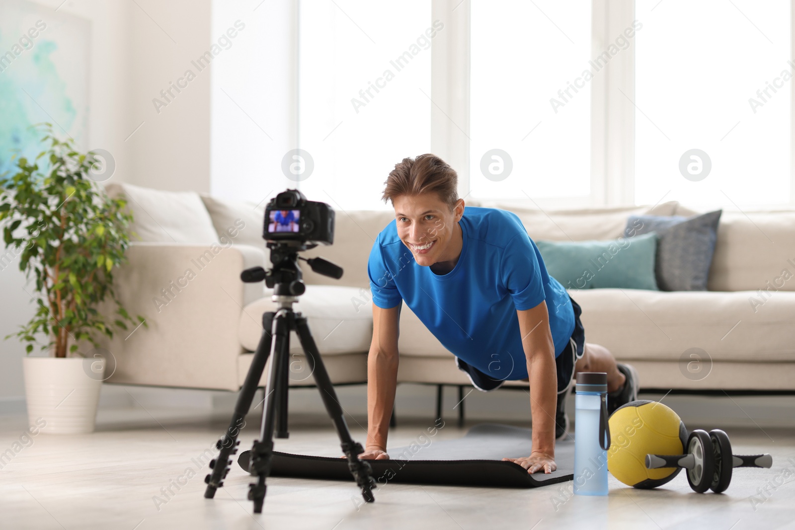 Photo of Smiling sports blogger recording fitness lesson with camera at home