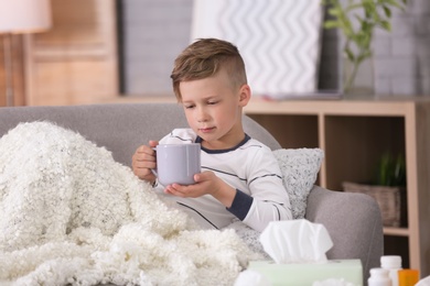 Photo of Little boy with cup of hot drink suffering from cold on sofa at home