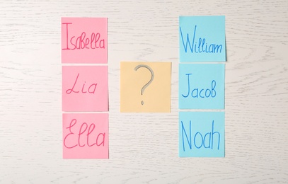 Colorful sticky notes with written baby names on white wooden background, flat lay