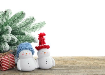 Photo of Cute decorative snowmen, gift box and fir tree on wooden table against white background, space for text