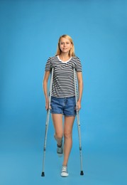 Young woman with axillary crutches on light blue background